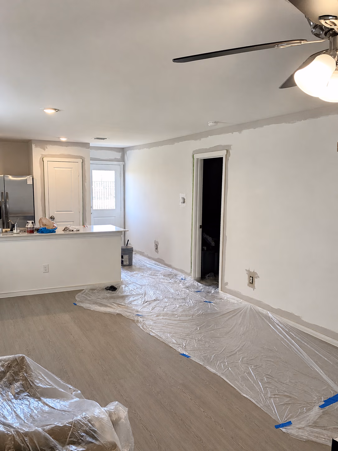 Living area with plastic covering floor and furniture, walls patched and prepped for painting.
