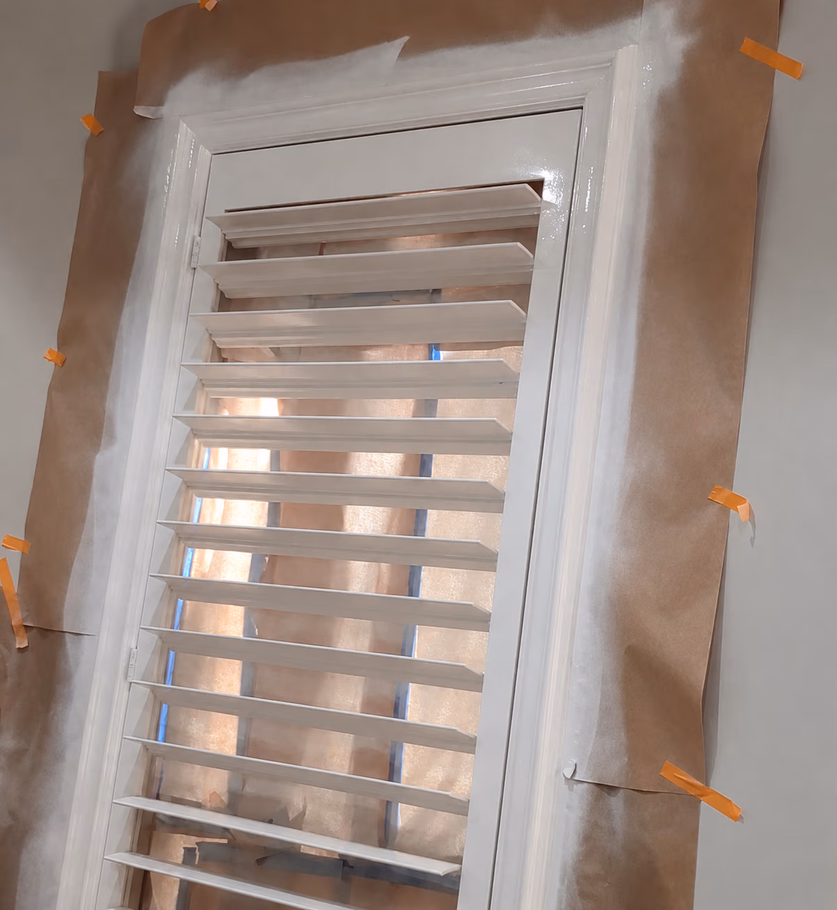 White plantation shutters installed on window with brown paper taped around the frame for painting.