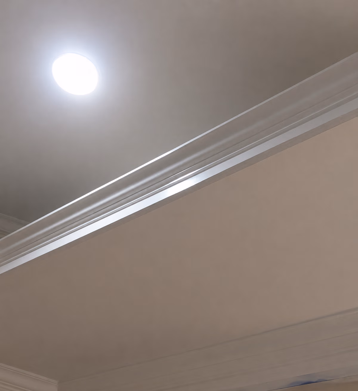 Bright ceiling light illuminating a beige wall with white crown molding.