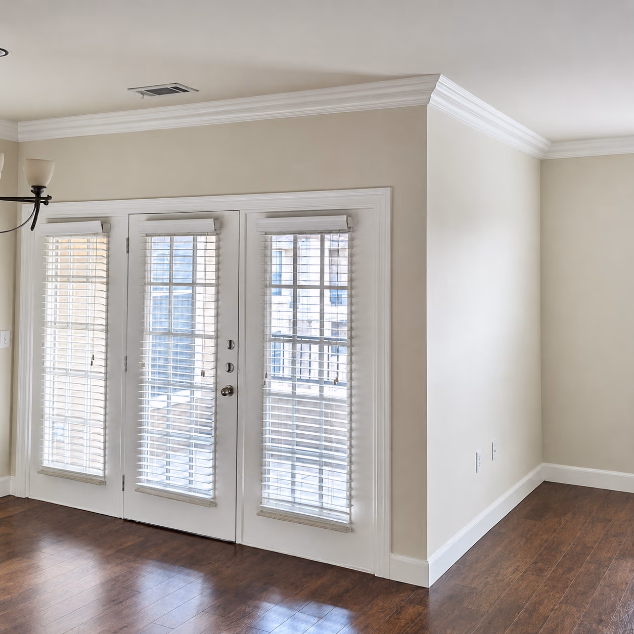 Empty room with wooden floor, beige walls, and white French doors with blinds.
