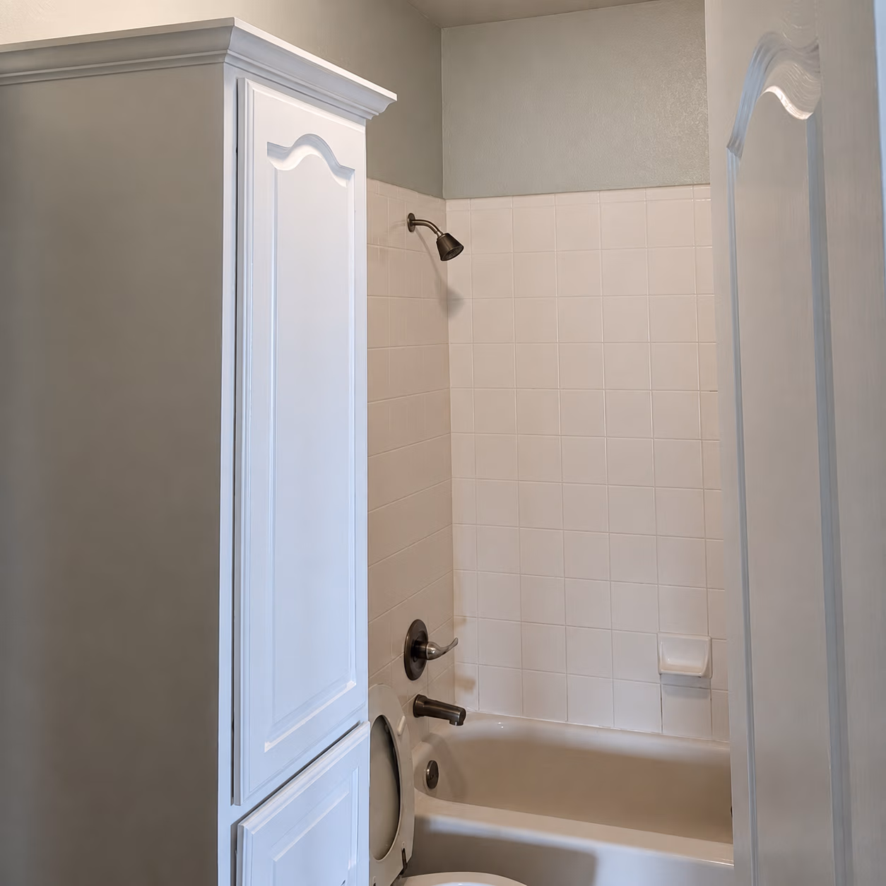 Bathtub with white tile walls, bronze shower fixtures, and a cabinet partially blocking view.