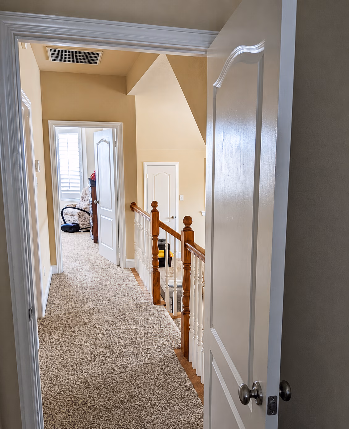 Carpeted hallway with white doors and wooden stair railing leading to rooms in a house.